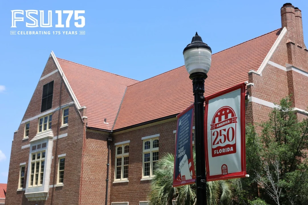 A brick building on a college campus stands under a clear blue sky, next to a lamppost adorned with celebratory banners for Florida and America.