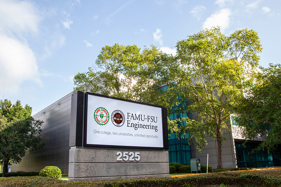 Photo of the FAMU-FSU College of Engineering sign in front of the building with a blue sky and green vegetation surrounding it.