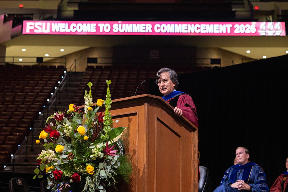 A speaker addresses an audience from a wooden podium during Florida State University's summer commencement ceremony.