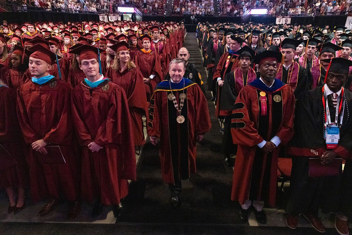 A university official leads a procession through rows of seated graduates during a commencement ceremony.