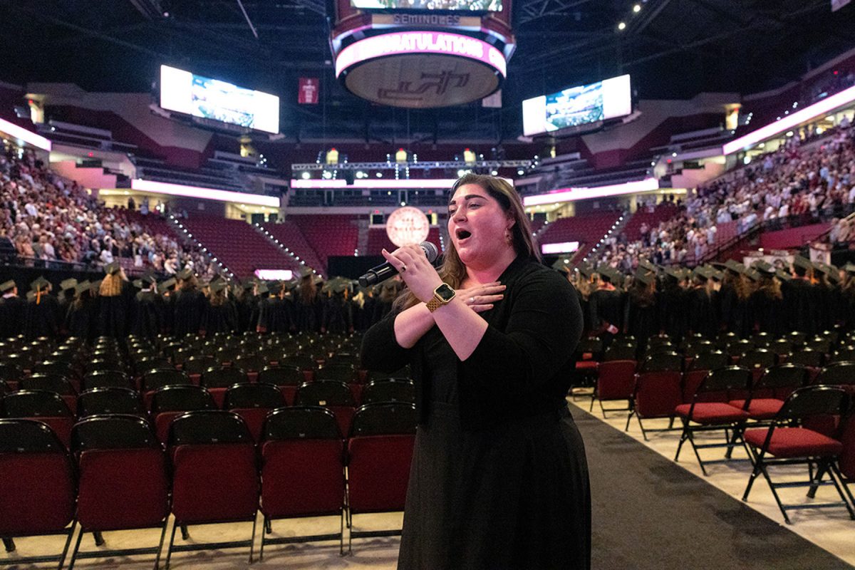 In a side-angle view, FSU Student Body President Ian Seibert addresses attendees from a flower-decorated podium during the commencement ceremony.