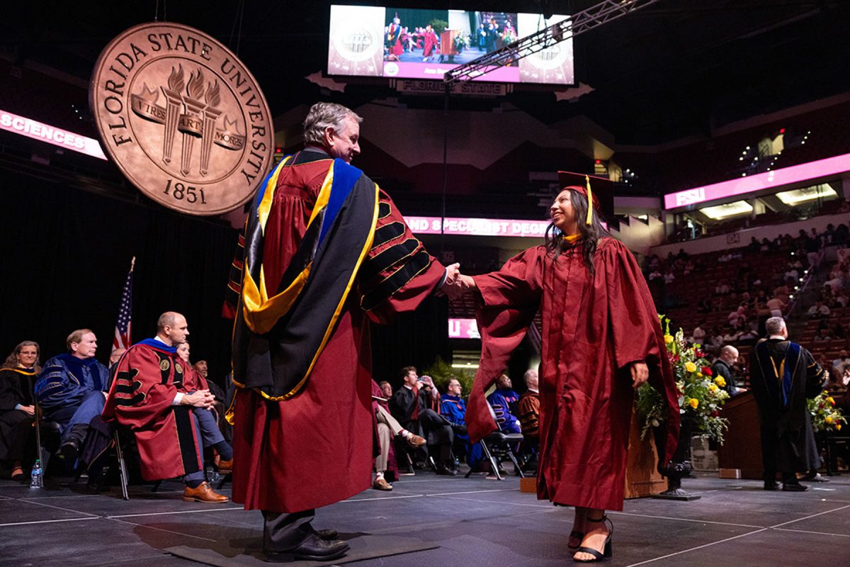 FSU President Richard McCullough shakes hands with a smiling graduate on stage beneath the large Florida State University seal.
