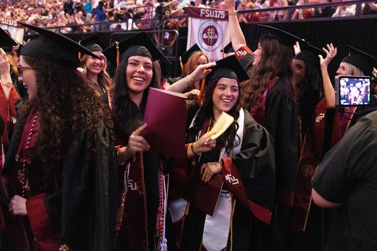 Joyful graduates celebrate, smile, and adjust each other's caps in a crowded section during the ceremony.