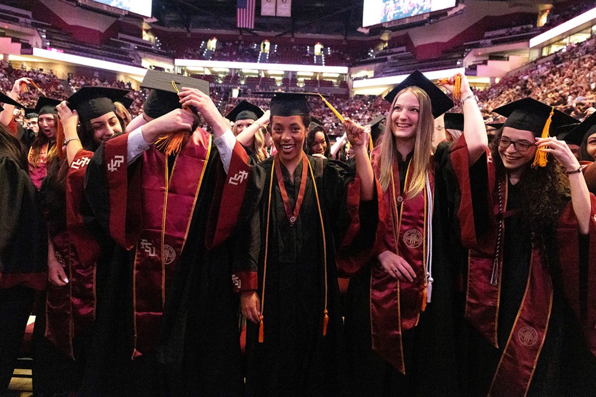 A group of smiling graduates celebrate together as they turn their tassels during the commencement ceremony.