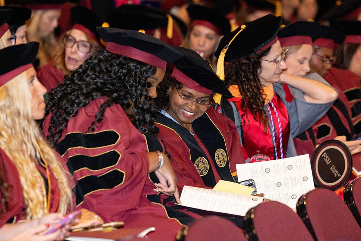 Two graduating candidates in caps and maroon gowns look through a commencement program together in the audience.