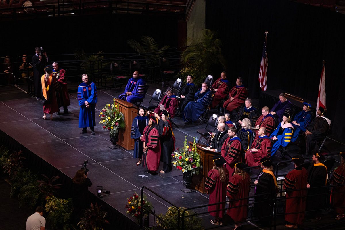 An elevated wide shot captures university faculty and graduates gathered on a stage during a commencement ceremony.