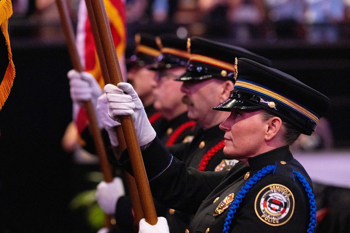 Members of the Seminole Tribe of Florida Color Guard, dressed in formal dress uniforms and white gloves, stand in a line holding flagpoles during a ceremonial presentation.