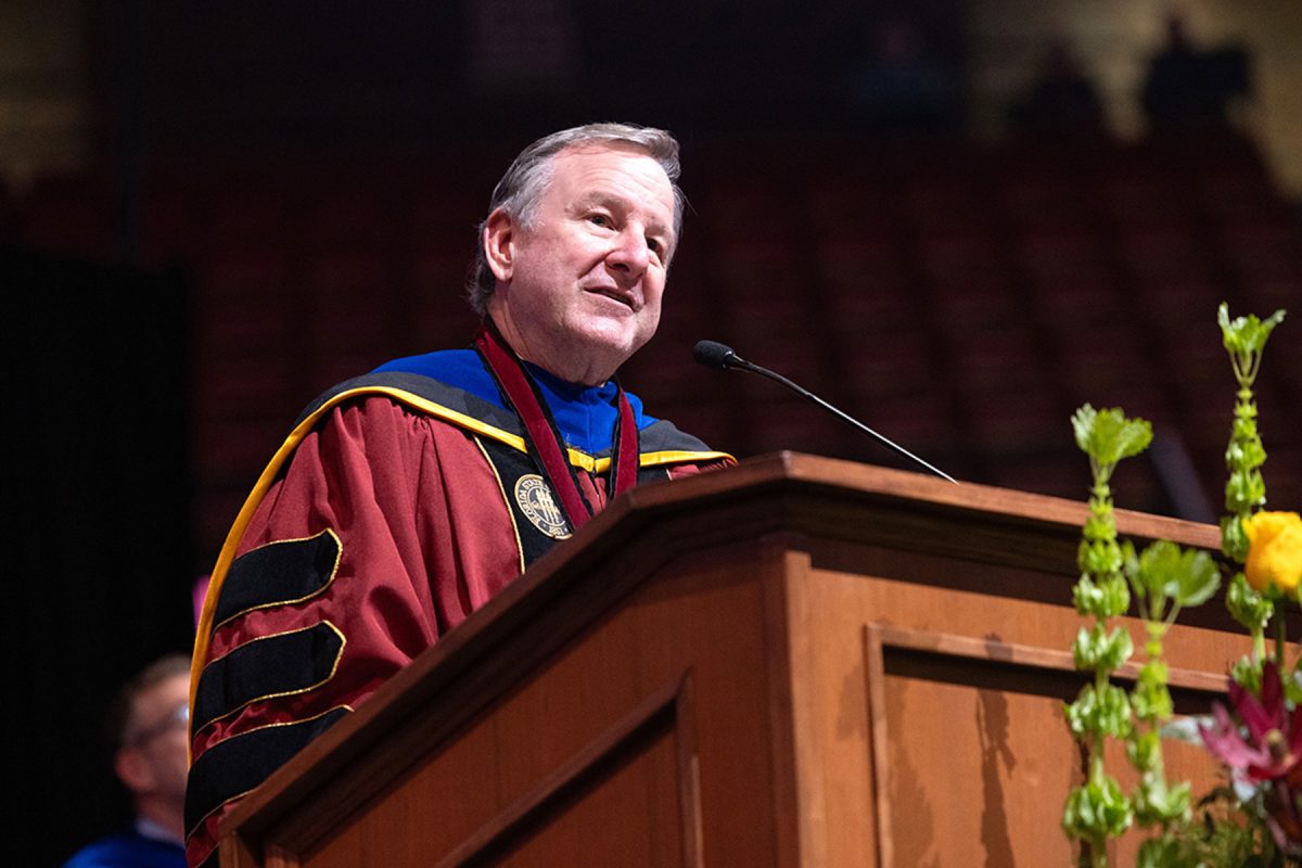 In a side-angle view, FSU Student Body President Ian Seibert addresses attendees from a flower-decorated podium during the commencement ceremony.