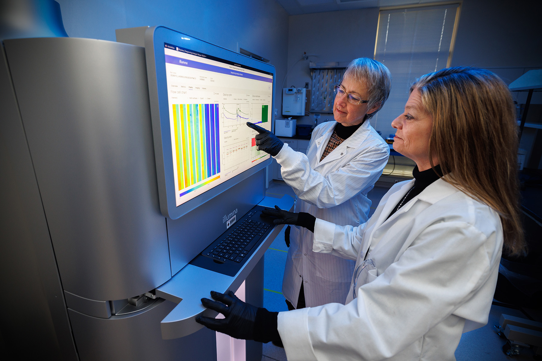 Two researchers review data on an Illumina NovaSeq X Plus DNA sequencing instrument.