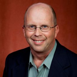 Man smiling in front of garnet backdrop.