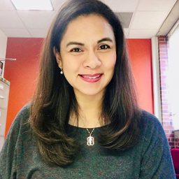 Mia Liza A. Lustria smiles for a photo in front of a red wall.