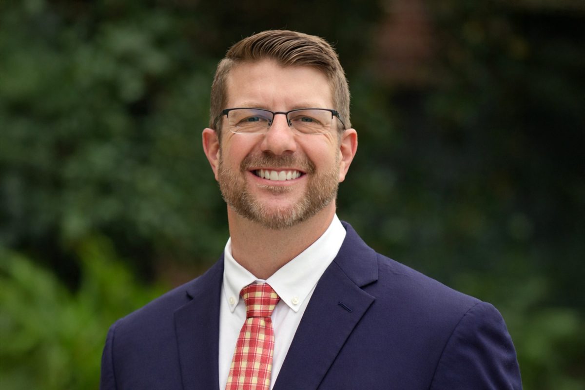 Portrait of a smiling man wearing glasses, a suit jacket, and a tie.