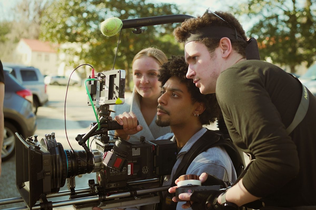 Three Florida State University film students gather around a professional digital cinema camera, reviewing footage on a monitor during an outdoor film production.