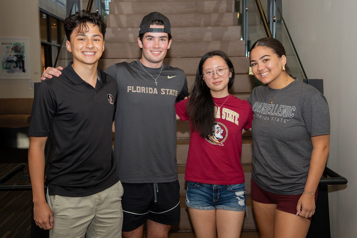 Two male and two female students link arms behind backs for a photo in front of a staircase.