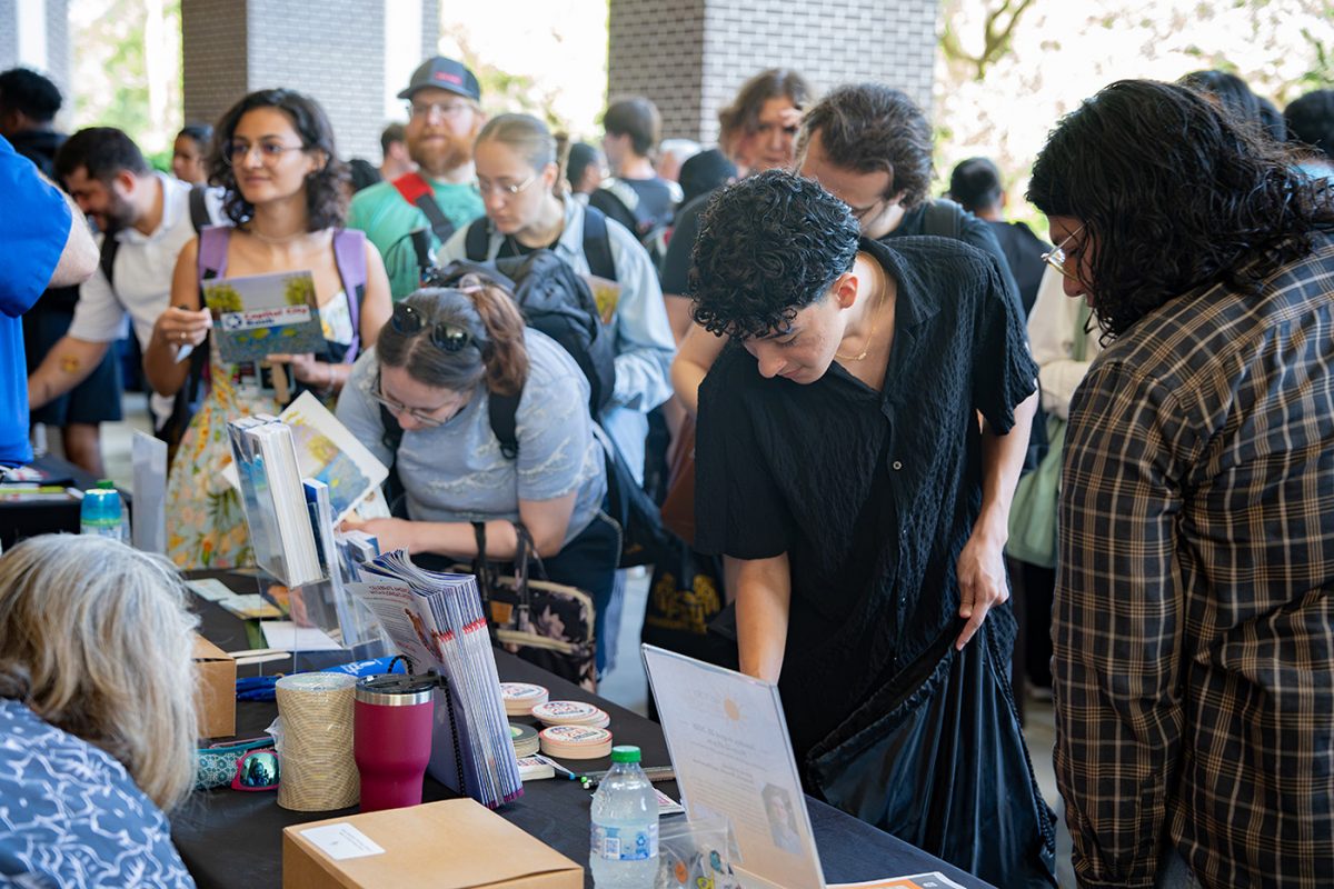 A male student in a black shirt reaches for an item on a table in a crowd of people.
