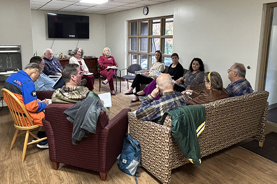 A group of a dozen people sitting in a circle in chairs.