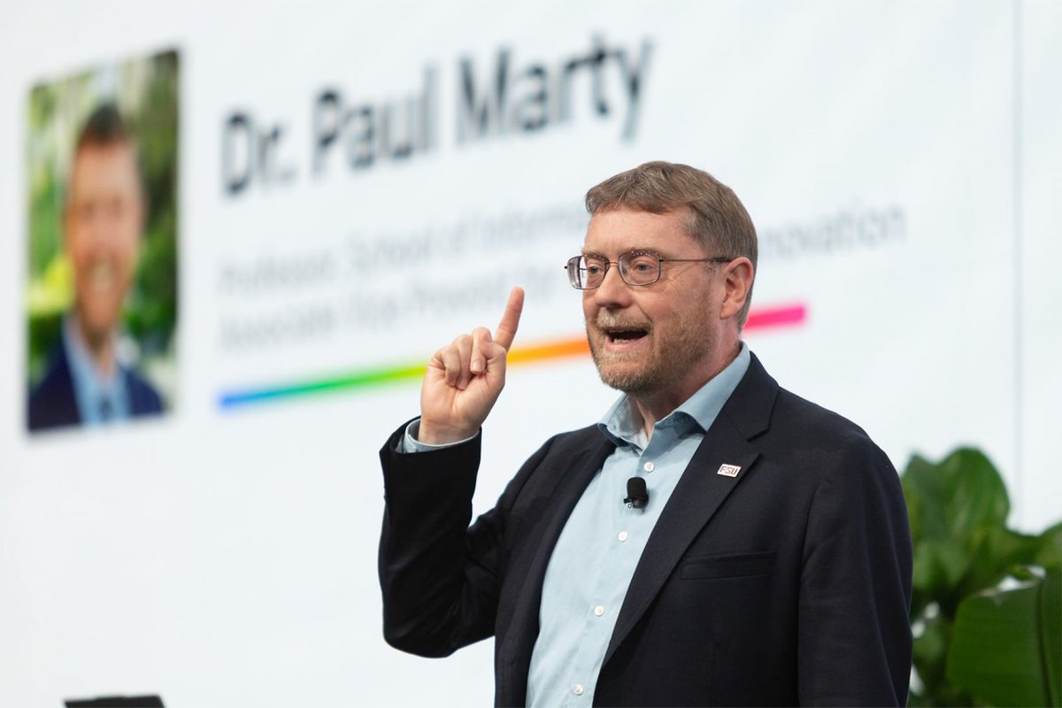 Paul Marty stands in front of a powerpoint slide with his name
