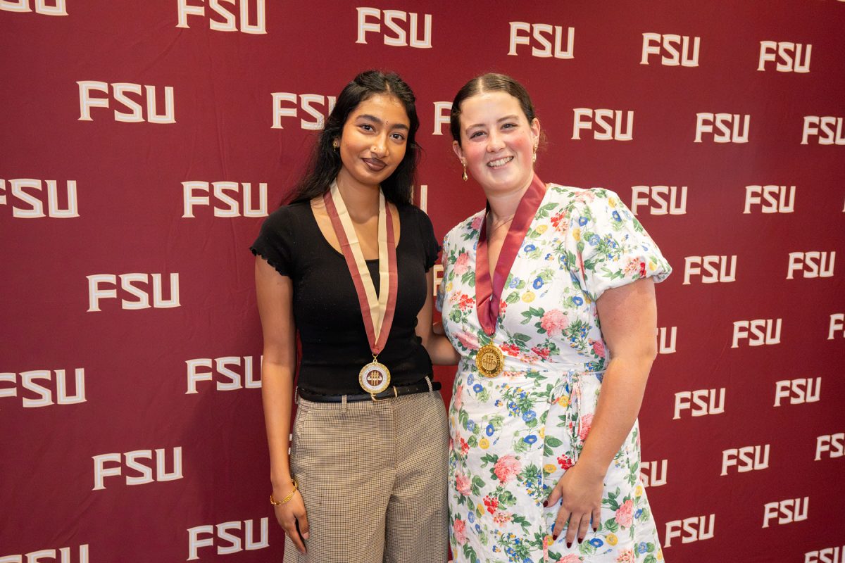 Two female summer 2026 honors graduates pose in front of an FSU backdrop.