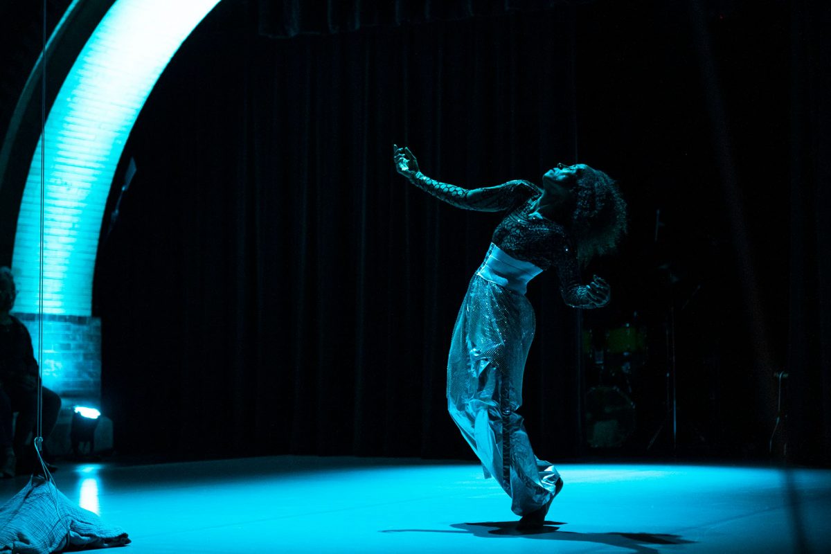 Dancer nia love reaches upward during a performance under blue stage lighting.