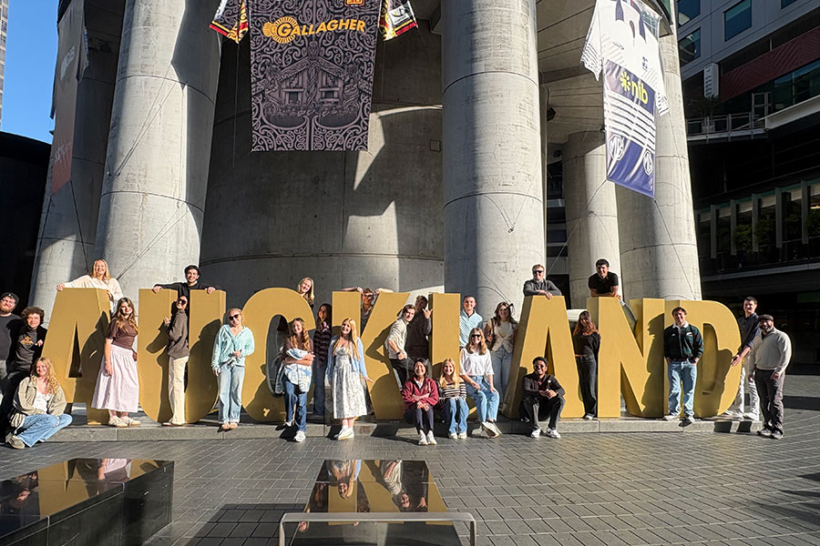 A group students scattered around a word statue spelling "Auckland" in New Zealand.