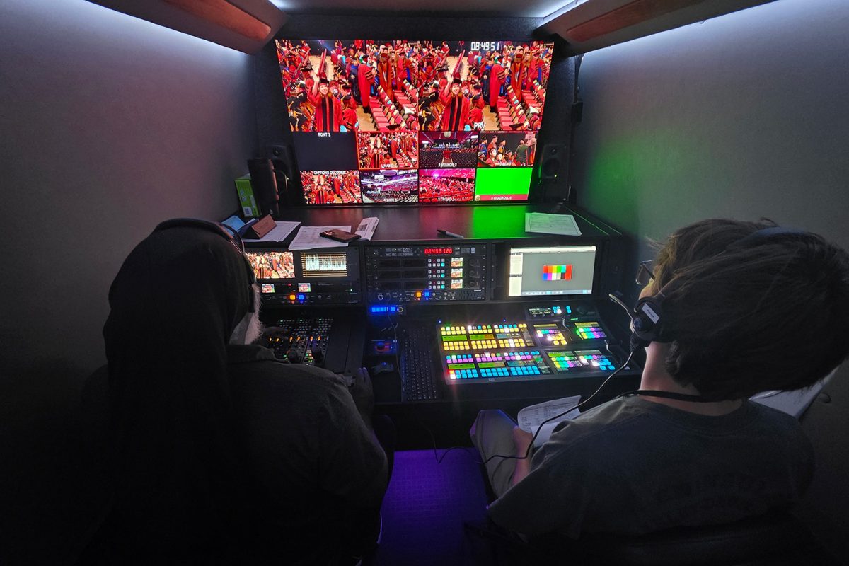 Two men look at a screen with livestreamed video.