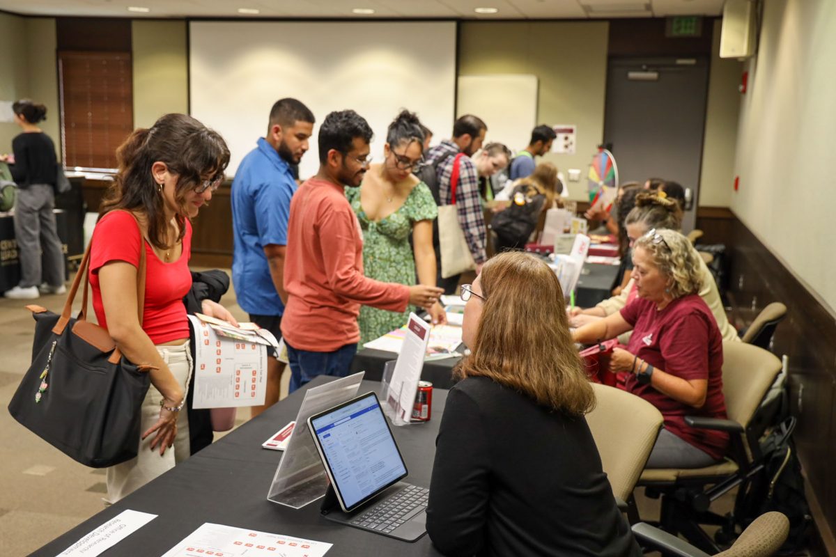 Students browse informational tables and speak with representatives at an indoor campus fair or orientation event.