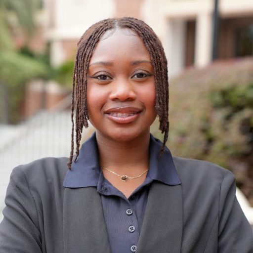 A woman wearing a grey suit and blue collared shirt posing for a headshot outside of the Westcott Building on FSU's Tallahassee campus.