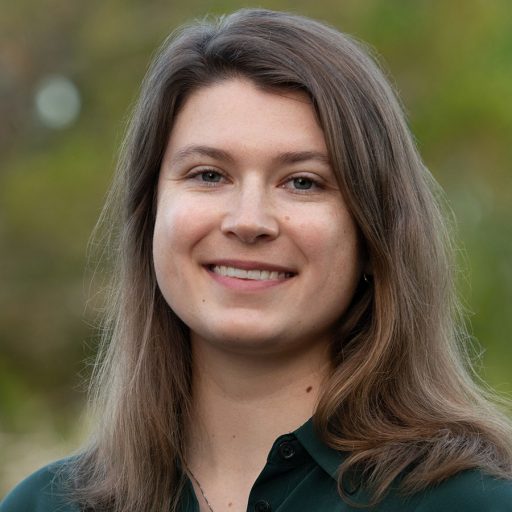 A woman poses for a headshot with out of focus greenery in the background.