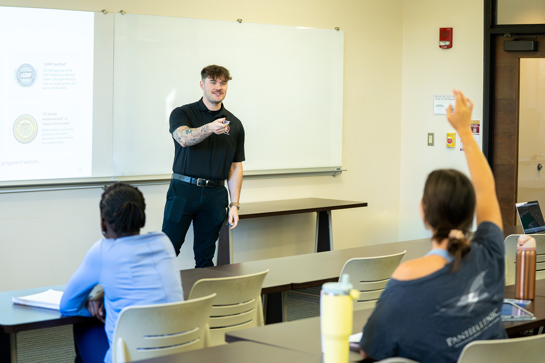 A instructor points toward a student raising their hand during a classroom presentation.