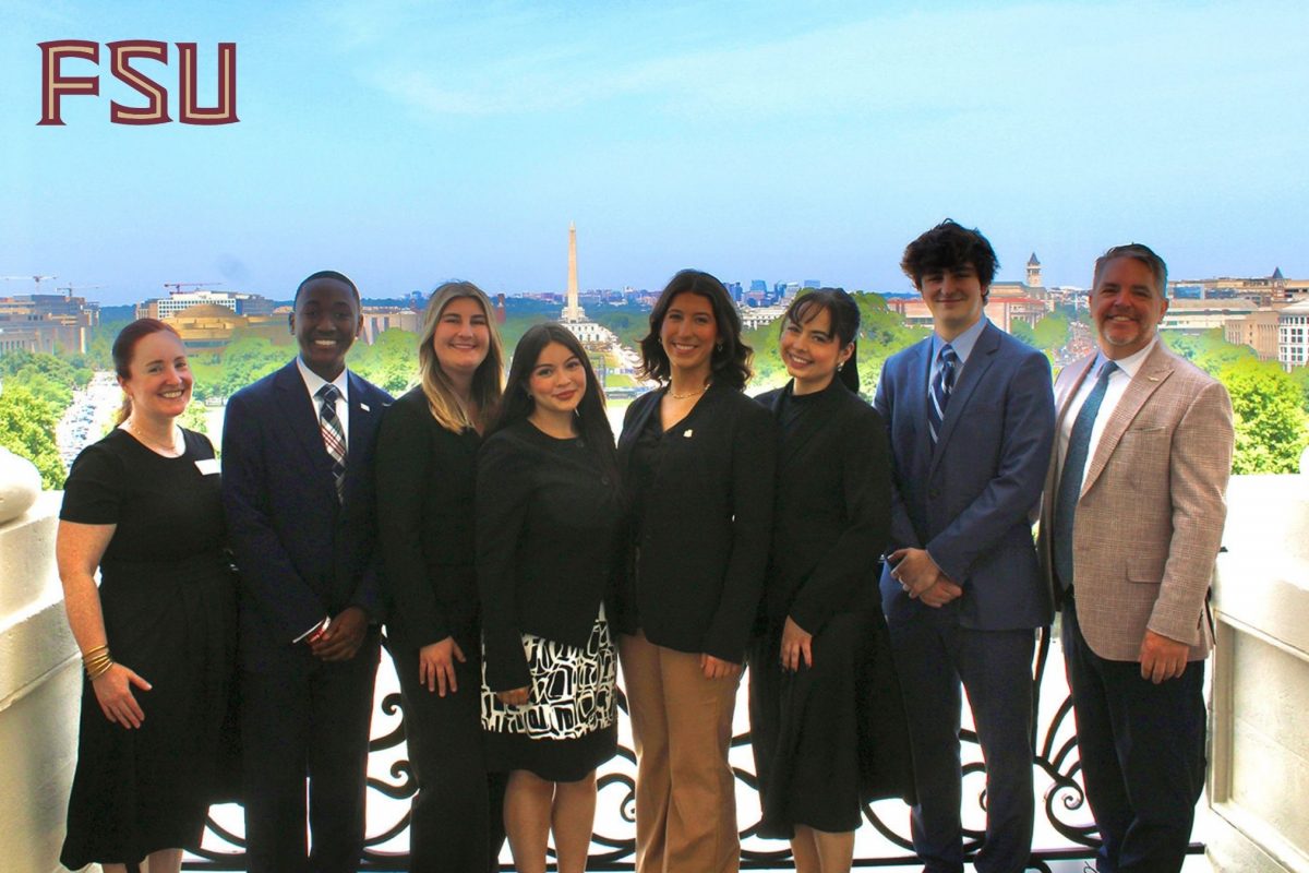 Eight people pose for a photo in professional clothing on a balcony overlooking the national mall in Washington, D.C.