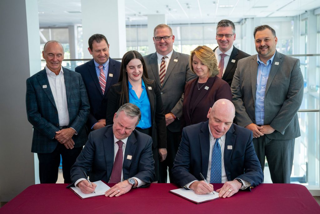 Florida State University and Tallahassee Memorial HealthCare leaders sign documents at a table with colleagues standing behind them.