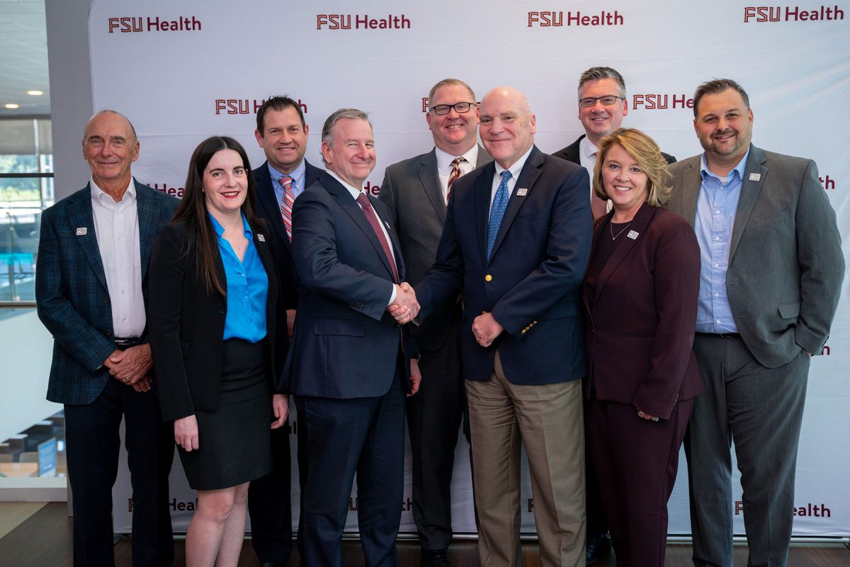 Florida State University and Tallahassee Memorial HealthCare leaders stand in front of a backdrop with the FSU Health logo.
