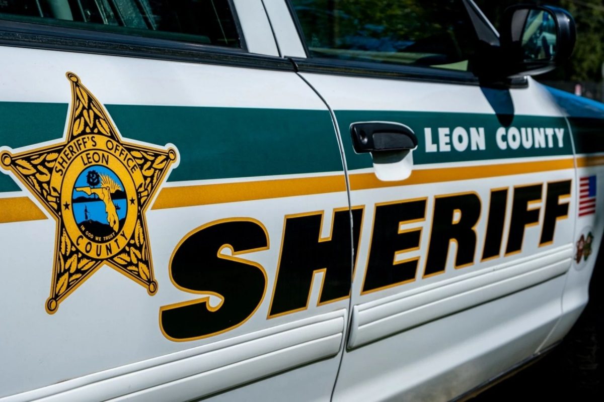 A close-up of the side door of a white Leon County Sheriff's Office patrol vehicle featuring the agency's gold star emblem and large "SHERIFF" lettering.