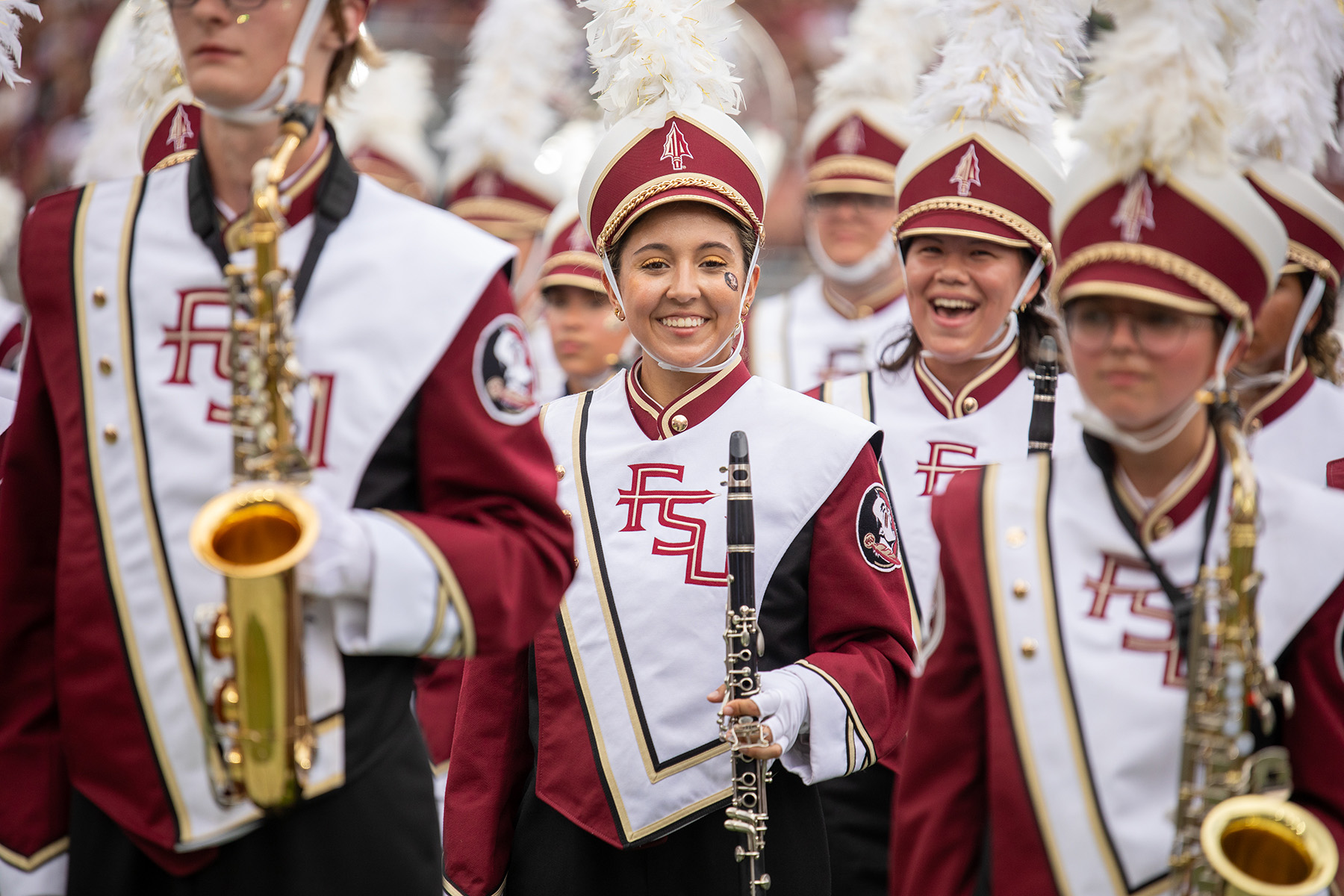 Members of the FSU Marching Chiefs in garnet-and-white uniforms smile while holding instruments.