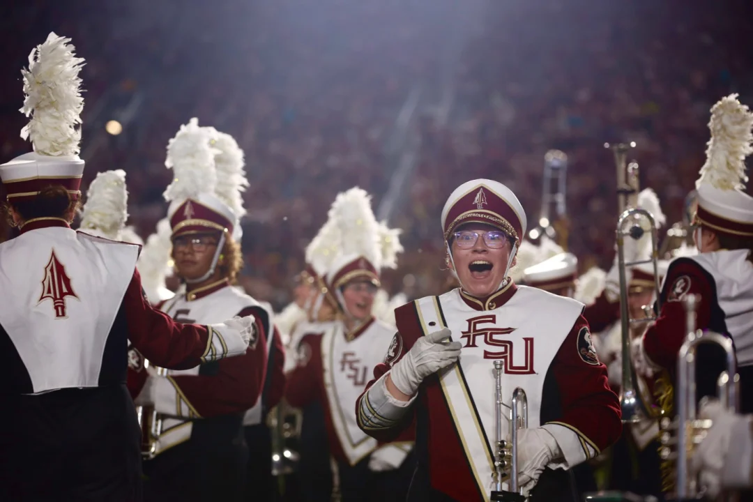 Members of the Florida State University marching band perform in uniform on the field during a stadium event.