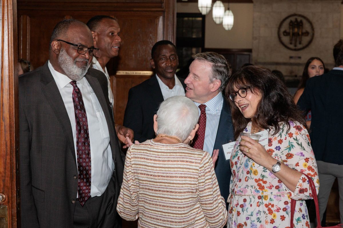 Odell Haggins, Jr. smiles while standing in a group of event attendees conversing during a reception.