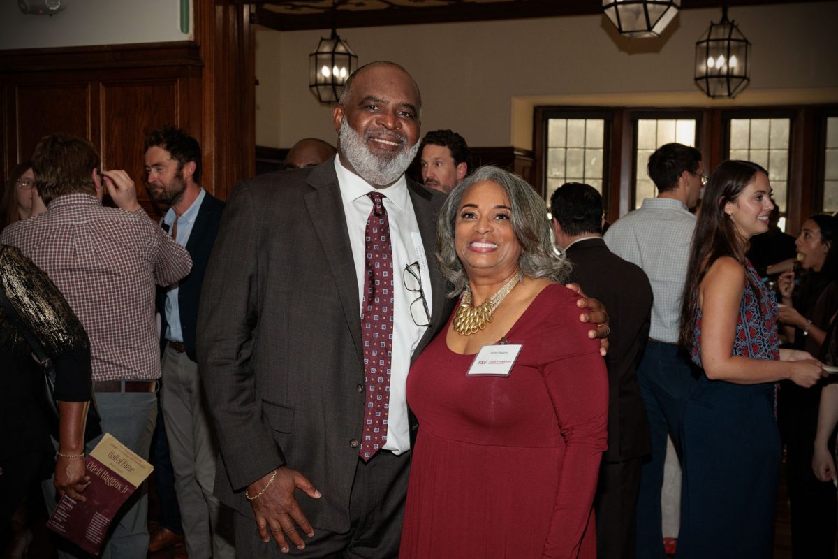 Odell Haggins, Jr. smiles while posing for a photo with a woman in a maroon dress in a crowded room.