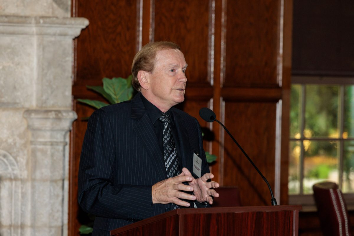 A man in a pinstripe suit gestures while speaking at a podium with a microphone.