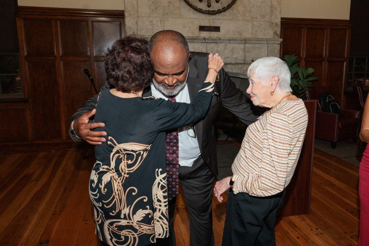 Odell Haggins, Jr. leans down to embrace a woman while another woman with short white hair looks on with a smile.