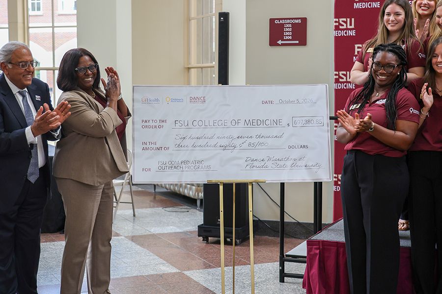 Attendees applaud around an oversized ceremonial check made payable to the FSU College of Medicine for $697,380.85. Dated Oct. 5, 2026, the check is from Dance Marathon at Florida State University and designates the funds for FSU College of Medicine pediatric outreach programs. Logos for UF Health Shands Children’s Hospital, Children’s Miracle Network Hospitals and Dance Marathon appear on the check.