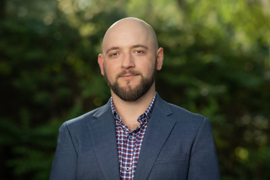 A photo portrait of Assistant Professor of Scientific Computing Hristo Chipilski wearing a sportcoat and standing in front of foliage.