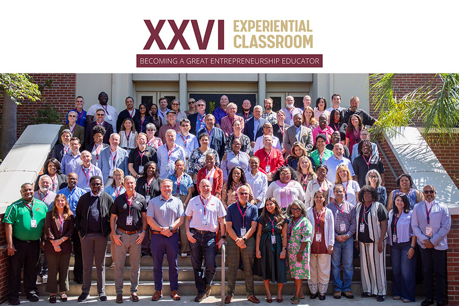 Large group of participants standing on outdoor steps beneath a sign for the 26th Experiential Classroom, an intensive entrepreneurship education professional development program.