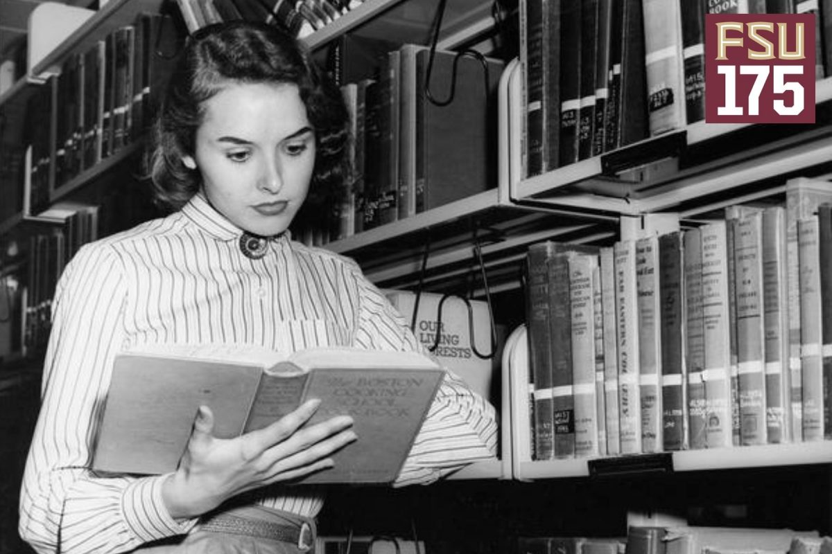 Female student in white striped blouse and skirt reads cookbook in Strozier Library stacks.