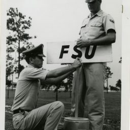 A black and white photo fo two male FSU cadets put up an FSU sign.