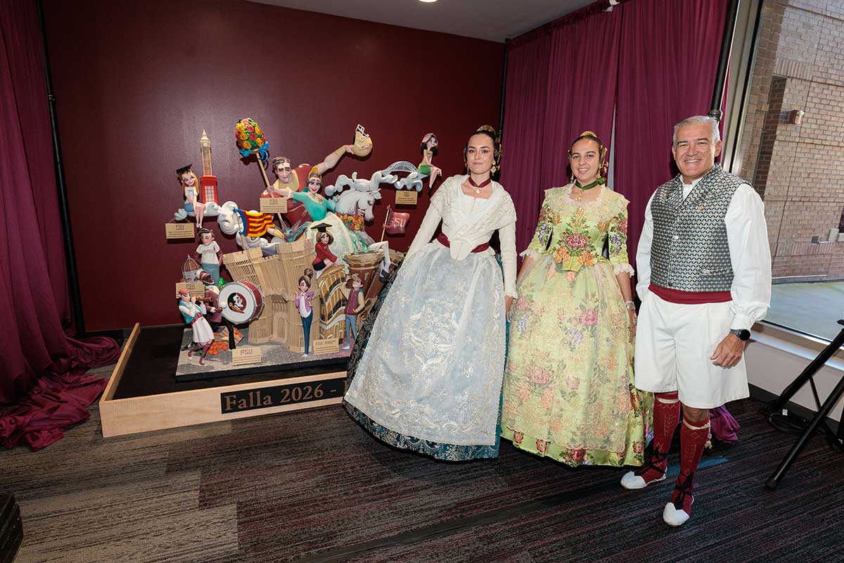 Three people pose in traditional Las Fallas festival clothing in front of a falla sculpture.