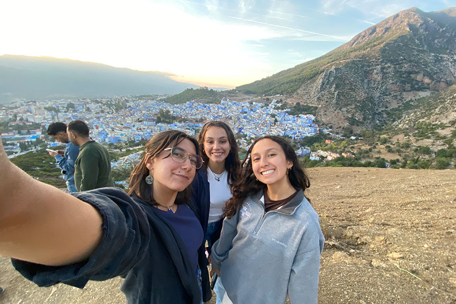 Three young women take a selfie with a mountain and city in the background.
