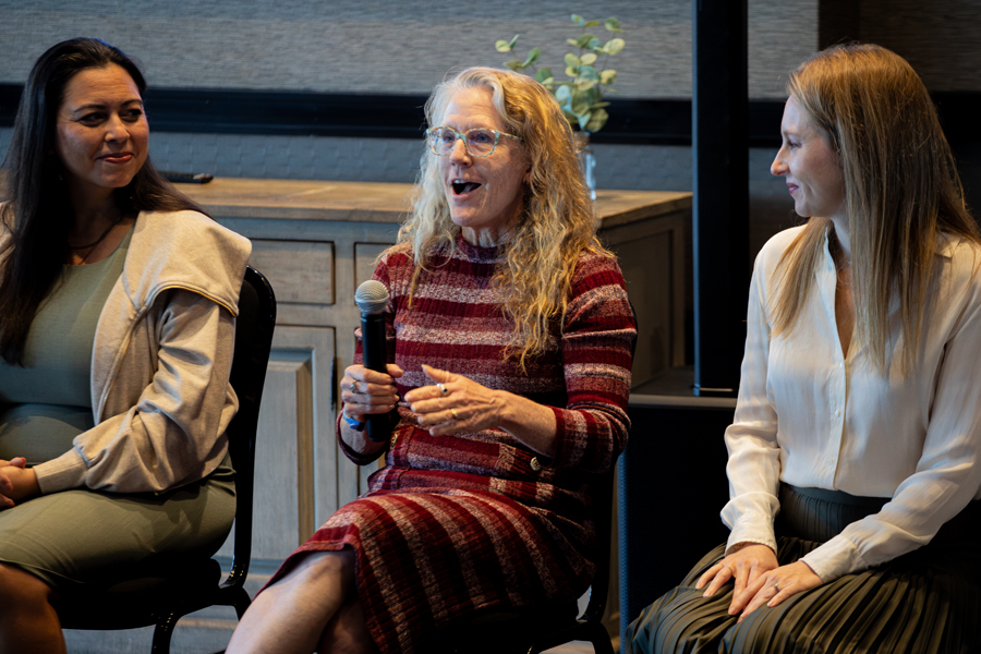 Three people sit on chairs. The person in the middle holds a microphone and speaks.