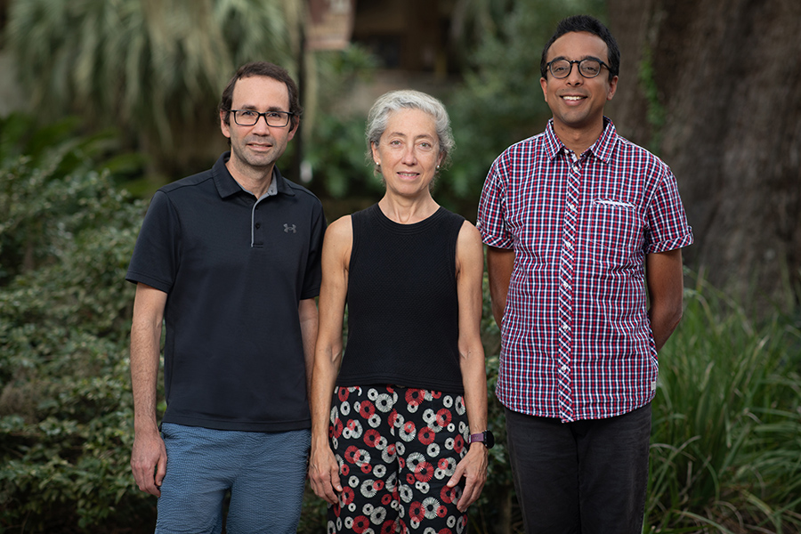 Three people standing for a photo portrait in front of foliage.
