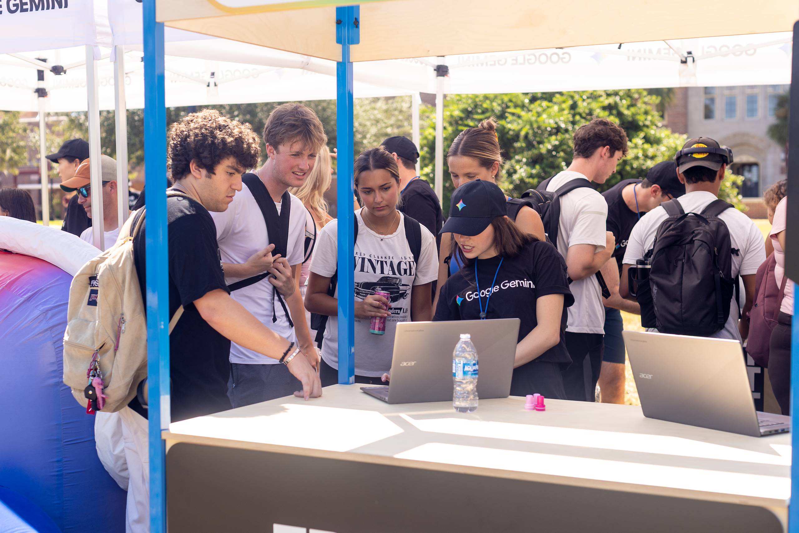 Students gather around a Google Gemini informational booth outdoors to interact with laptops and staff.