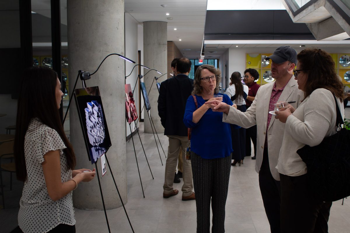 Attendees at an exhibition gather around display easels illuminated by spotlights to view and discuss scientific photos on display in a modern building hallway. (Isa Velazquez/Florida State University)